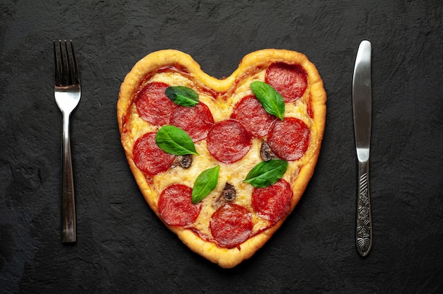 Herzförmige Pizza auf einem schwarzen Stein. Romantisches Liebeskonzept zum Valentinstag