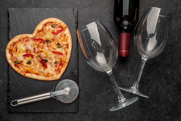 Herzförmige Pizza zum Valentinstag mit einer Flasche Wein und zwei Gläsern auf Schiefer