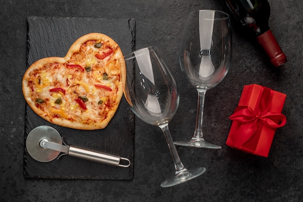 Herzförmige Pizza zum Valentinstag mit einer Flasche Wein und zwei Gläsern auf Schiefer