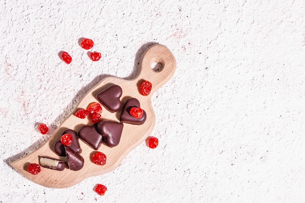 Herzförmige Pralinen mit getrockneten Kirschen. Modernes hartes Licht, dunkler Schatten. Ein süßes Geschenk zum Valentinstag oder Jubiläum. Helle Töne Gips Hintergrund, Ansicht von oben