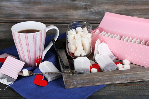 Herzförmige Teebeuteletiketten, Schachtel und Tasse Tee auf Holzhintergrund