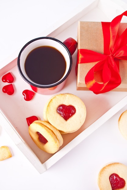 Herzförmige traditionelle Linzer-Kekse mit Erdbeermarmelade, Tasse Kaffee und Geschenkbox
