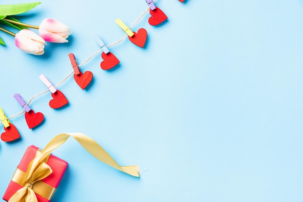 Herzförmige Valentinsdekoration, die mit Clips für die Liebe und rote Geschenkbox hängt