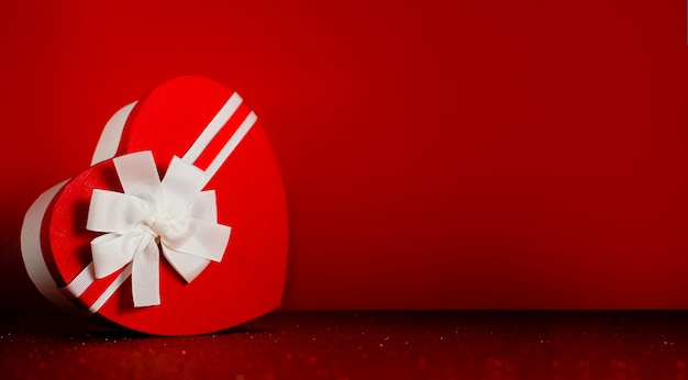 Herzförmiger Kasten mit rotem funkelndem Hintergrund des Bandes. Valentinstag und Engagement-Konzept.