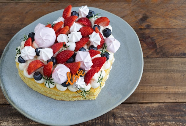 Herzförmiger Kuchen mit roten Früchten und Baiser dekoriert Holzsockel Valentinstag Kopierbereich