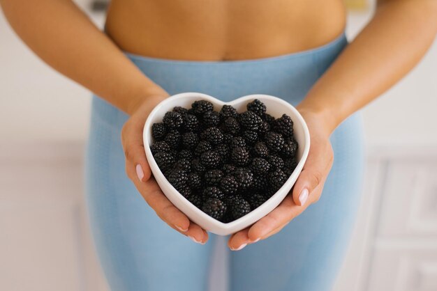 Herzförmiger Teller mit Brombeeren in Frauenhänden das Konzept der gesunden Ernährung