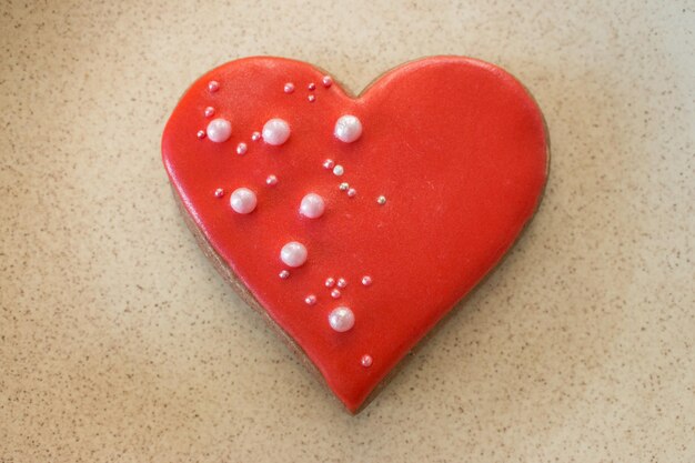 Herzförmiges Lebkuchenplätzchen auf beigem Hintergrund. Süßer roter Herzkeks. Valentinstag dekor.