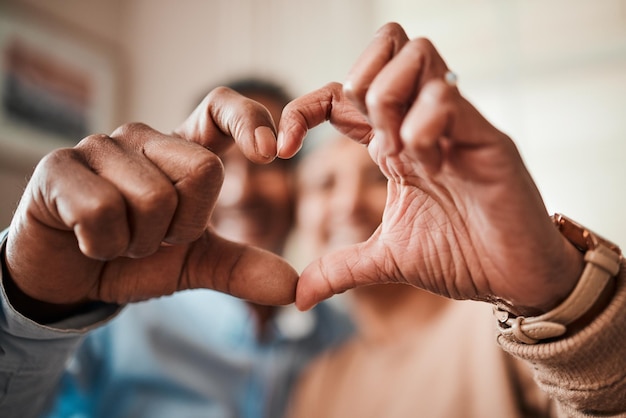 Herzform und Hände eines älteren Paares zu Hause mit Liebe, Glück und Fürsorge. Mann und Frau entspannen sich gemeinsam mit einem Symbol oder Emoji für die Verpflichtung, Ehe und Vertrauen oder Unterstützung am Valentinstag