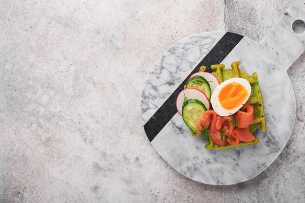 Herzhafte Waffeln Frühstück grüne Waffeln Bärlauch oder Spinat mit Ei Tomate Lachs auf Teller zum Frühstück auf grauem Betontisch Hintergrund Leichtes Abendessen Mittag- oder Frühstück Draufsicht Mock up