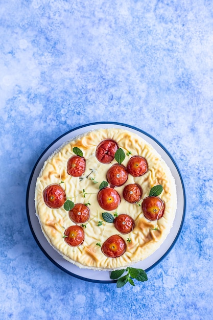 Herzhafter Käsekuchen mit Tomaten, dekoriert mit Minze, blauer Betonhintergrund. Ansicht von oben.