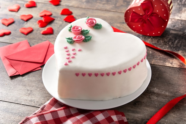 Herzkuchen zum Valentinstag, verziert mit Rosen und rosa Zuckerherzen auf Holztisch