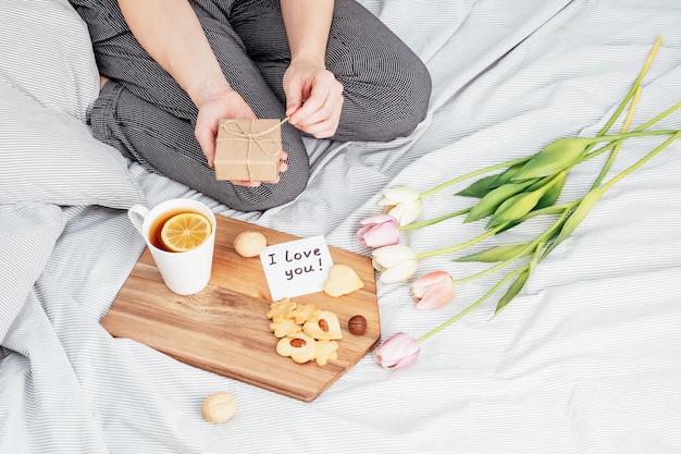 Herzlichen Glückwunsch an Ihr Lieblingsmädchen zum Valentinstag. Frühstück im Bett. Eine Frau im Pyjama nimmt am 14. Februar Geschenke an.