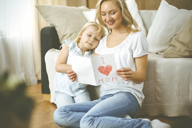 Herzlichen Glückwunsch zum Muttertag. Die kleine Tochter gratuliert der Mutter und gibt ihr eine Postkarte mit Herzzeichnung. Familien- und Kindheitskonzepte.