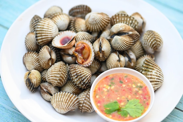 Herzmuscheln auf weißem Teller mit Meeresfrüchte-Sauce auf Tischhintergrund Frische rohe Schalentiere Blut Herzmuschel Ozean Gourmet-Meeresfrüchte im Restaurant