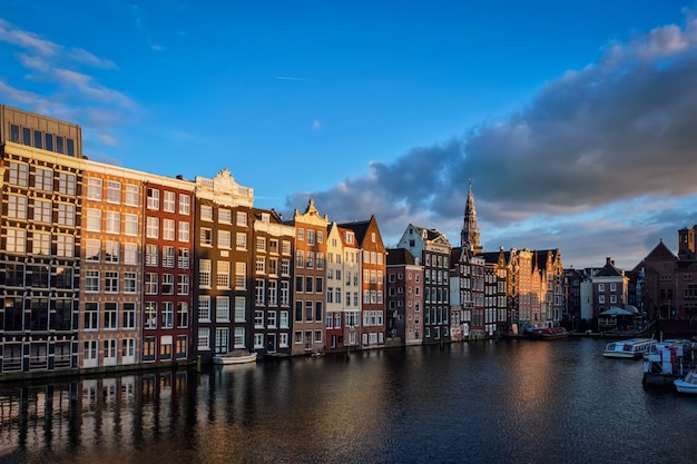 Hhouses e barcos turísticos no cais do canal de Amsterdã Damrak em sóis