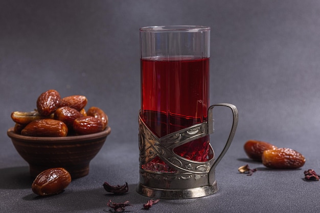 Hibiscus heißer Tee mit Datteln Traditioneller Ramadan Kareem Konzept Snack für Iftar oder Suhoor Mahlzeit auf dunklem Stein Beton Hintergrund Eine arabische süße Behandlung hartes Licht dunkler Schatten Kopierraum