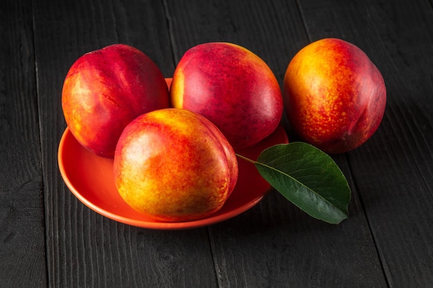 Los híbridos de nectarina roja madura en su temporada de maduración se encuentran en un plato naranja o en una mesa vintage oscura