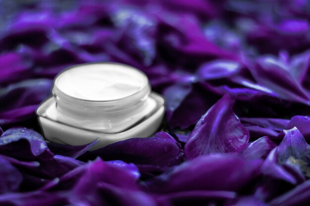 Foto hidratante de crema facial de lujo para la piel facial sobre fondo de flores moradas cosméticos de spa floral essense y emulsión de belleza para productos de marca para el cuidado de la piel