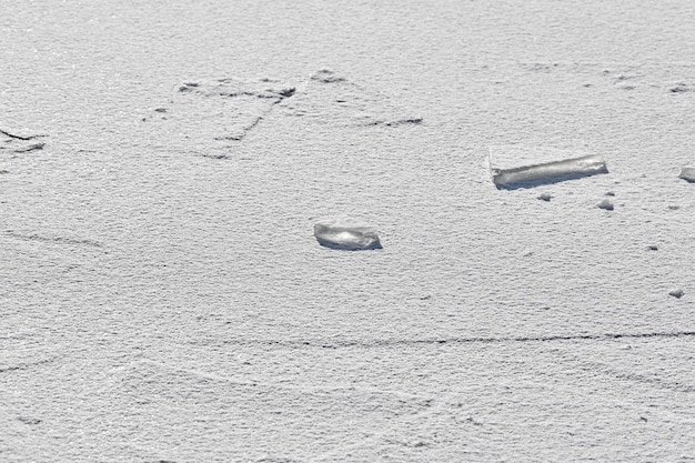 Hielo agrietado del lago congelado con nieve blanca en la parte superior. Fondo de textura de hielo, de cerca.