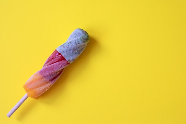 Hielo de frutas de colores en un palo de madera sobre una superficie de color amarillo brillante Concepto de comida de verano