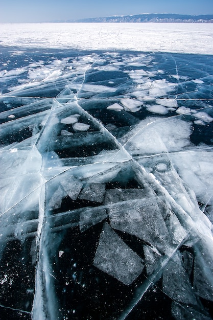 Hielo oscuro transparente en el lago Baikal con trozos de hielo congelados y grandes grietas hermosas
