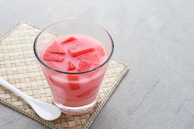 Hielo de sandía fresca con jarabe y leche servido en vaso sobre fondo gris