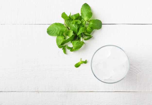 Hielo en un vaso y menta fresca sobre una madera blanca