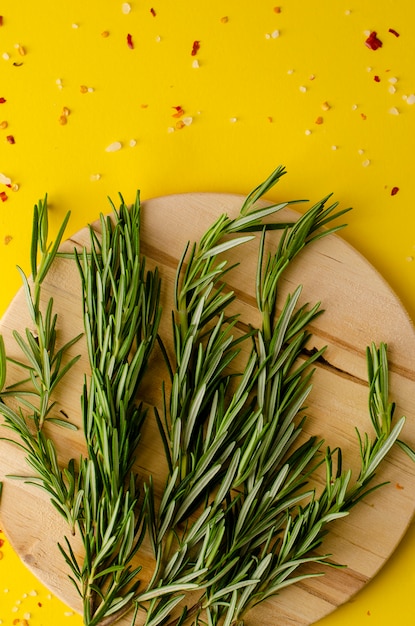 Hierbas frescas del romero en la tabla de cortar de madera en fondo amarillo