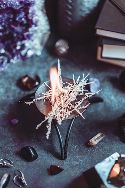 Foto hierbas quemadas en el altar de una bruja para un ritual mágico entre cristales y velas negras