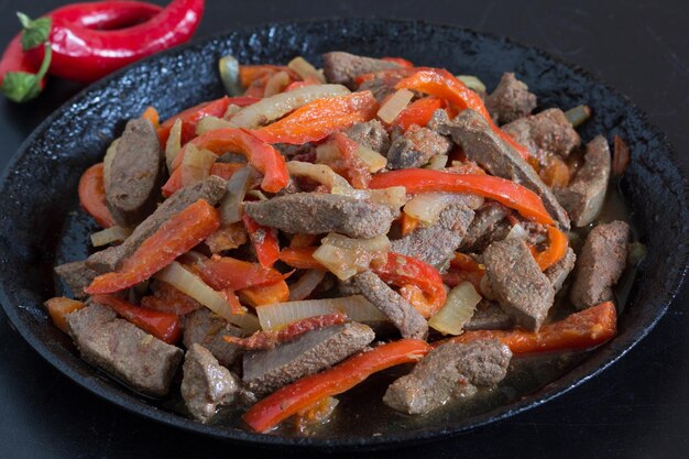 Hígado cocido con verduras en sartén sobre fondo negro