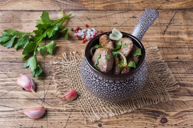 Hígado de pollo cocido con la cebolla en un cocotte de cerámica en una tabla rústica de madera.