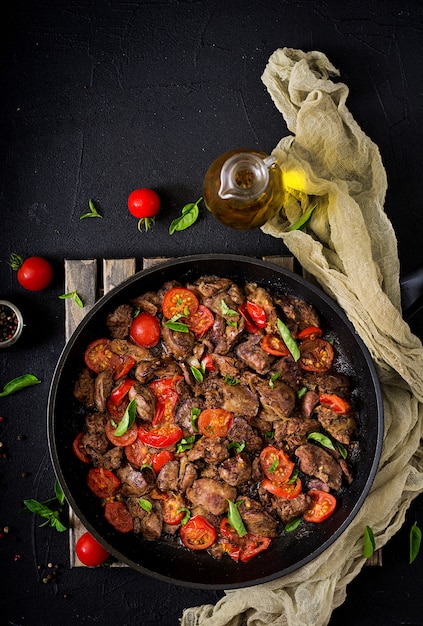 Hígado de pollo (despojos) con cebolla y tomate en una sartén en armenio. Endecha plana. Vista superior