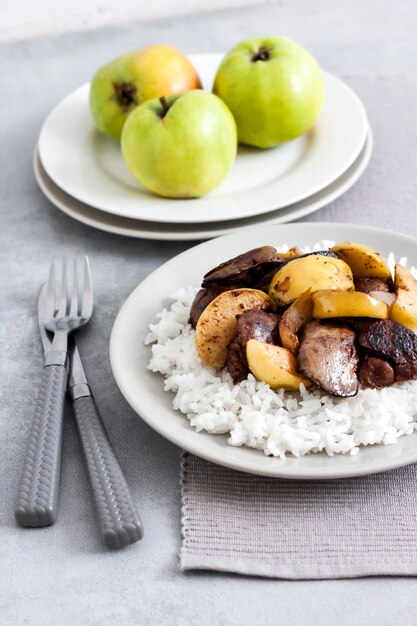 Hígado de pollo frito con manzanas servido con arroz blanco en un plato. Manzanas verdes sobre fondo