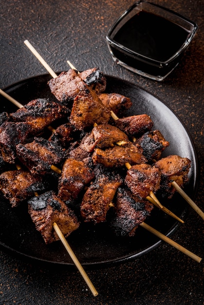 Hígado de res a la parrilla en brochetas, con teriyaki o salsa de soja, yakitori, vista de mesa oxidada oscura