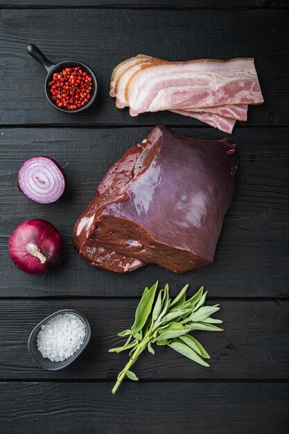 Hígado de res con tocino y cebolla sobre fondo de madera negra, vista superior.