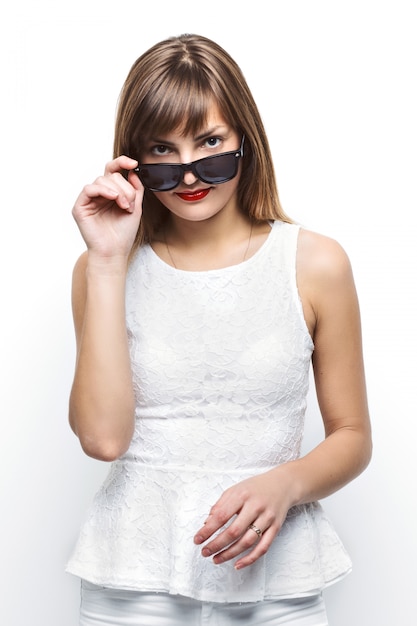 High Fashion Look.glamour stilvoll Schönes junges weibliches Modell mit roten Lippen in weißen Sommer hellen bunten Stoff und Hipster Sonnenbrille.