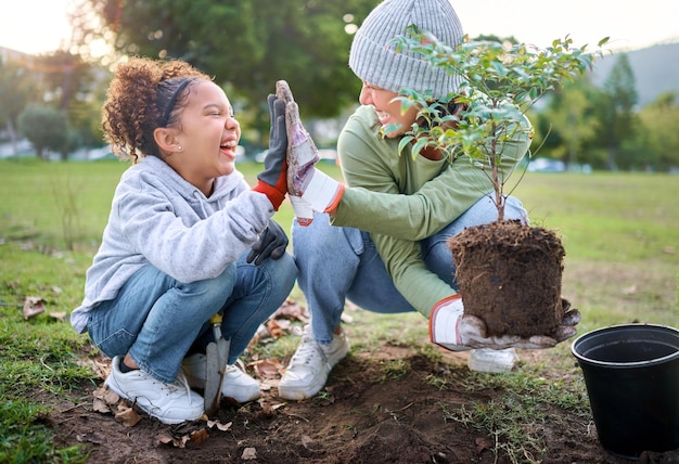 High Five Kind und Frau mit Pflanze für die Gartenarbeit im Park mit Bäumen in der Naturgartenumgebung Fröhliche freiwillige Familienpflanzung für Wachstumsökologie und Nachhaltigkeit für die Gemeinschaft am Tag der Erde