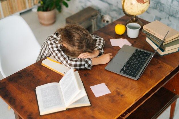 Highangle vista de niña de la escuela niño cansado durmiendo en la mesa de trabajo acostado en portátiles agotado