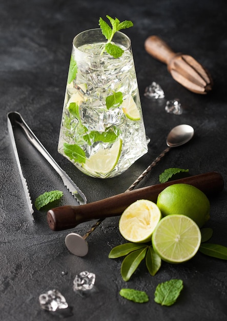 Highball-Glas Mojito-Cocktail mit Eiswürfeln, Minze und Limette auf schwarzem Brett mit Löffel