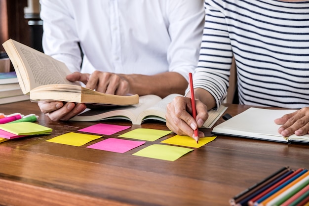 Highschool- oder Student-Gruppe, die am Schreibtisch in der studierenden und lesenden Bibliothek sitzt, Hausaufgaben macht und Lektion üben