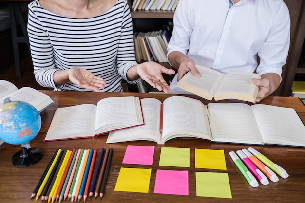 Highschool- oder Student-Gruppe, die am Schreibtisch in der studierenden und lesenden Bibliothek sitzt, Hausaufgaben macht und Lektion üben