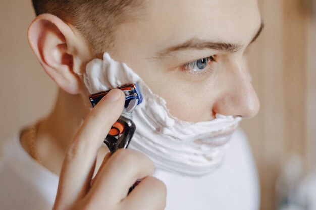 Higiene da manhã, o homem faz a barba com espuma