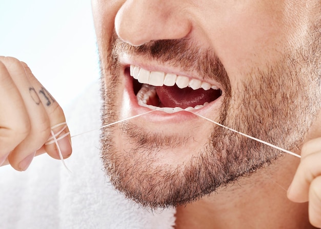 Higiene dental e homem passando fio dental em um estúdio para higiene bucal ou saúde Bem-estar saudável e close-up do modelo masculino fazendo rotina de boca limpa e natural fresca por fundo branco