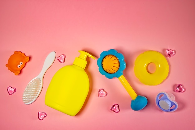 Foto higiene infantil: artículos de baño, botella de champú, juguete de goma, esponja, peine, termómetro, tijeras de seguridad vista superior, sobre fondo rosa. kit de cuidado personal para niños. accesorios de baño.