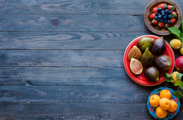 Higos frescos con duraznos, albaricoques, arándanos, fresas, sobre una superficie de madera.