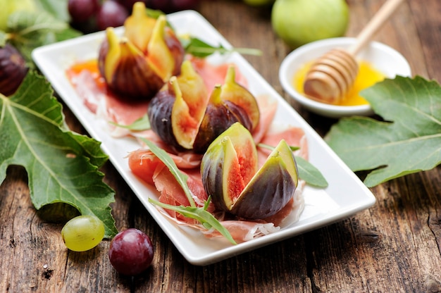 Higos frescos con jamón en una placa blanca.