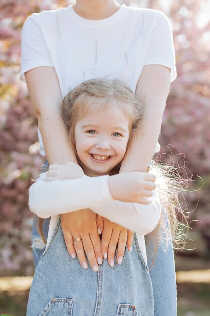 La hija abraza las manos de su madre en el parque cerca del sakura.
