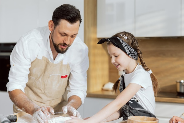 La hija de Adorabla pasa tiempo con el padre joven en la cocina moderna preparando pizza casera