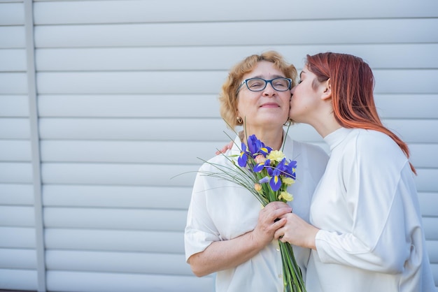 La hija adulta le da flores a su madre afuera en el patio de la casa Pasar tiempo juntos celebrando en casa los fines de semana Día de la Madre Cálidas relaciones intergeneracionales