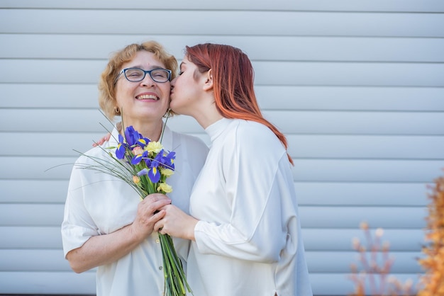 La hija adulta le da flores a su madre afuera en el patio de la casa Pasar tiempo juntos celebrando en casa los fines de semana Día de la Madre Cálidas relaciones intergeneracionales